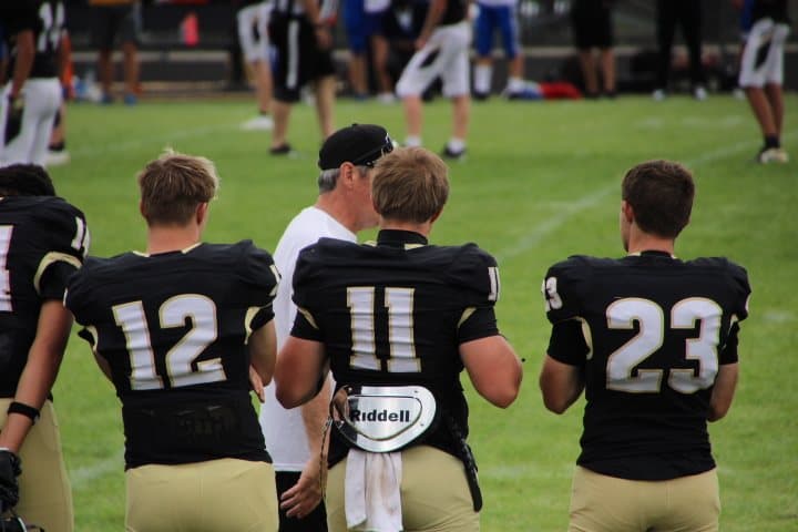 Football players in black and gold talking with a coach on the sideline