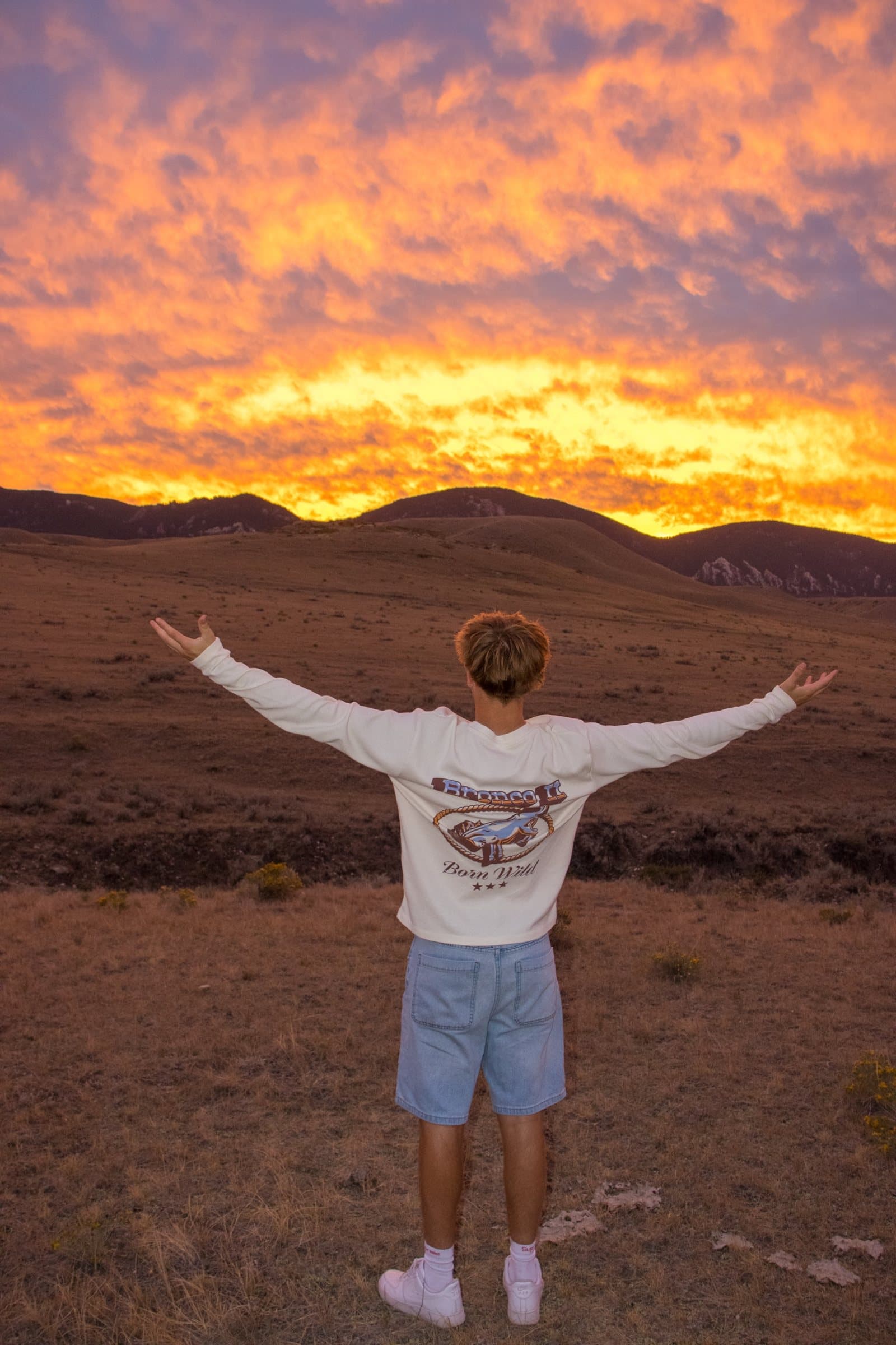 Senior portrait from behind, arms open to a fiery sunset over the Bighorn foothills