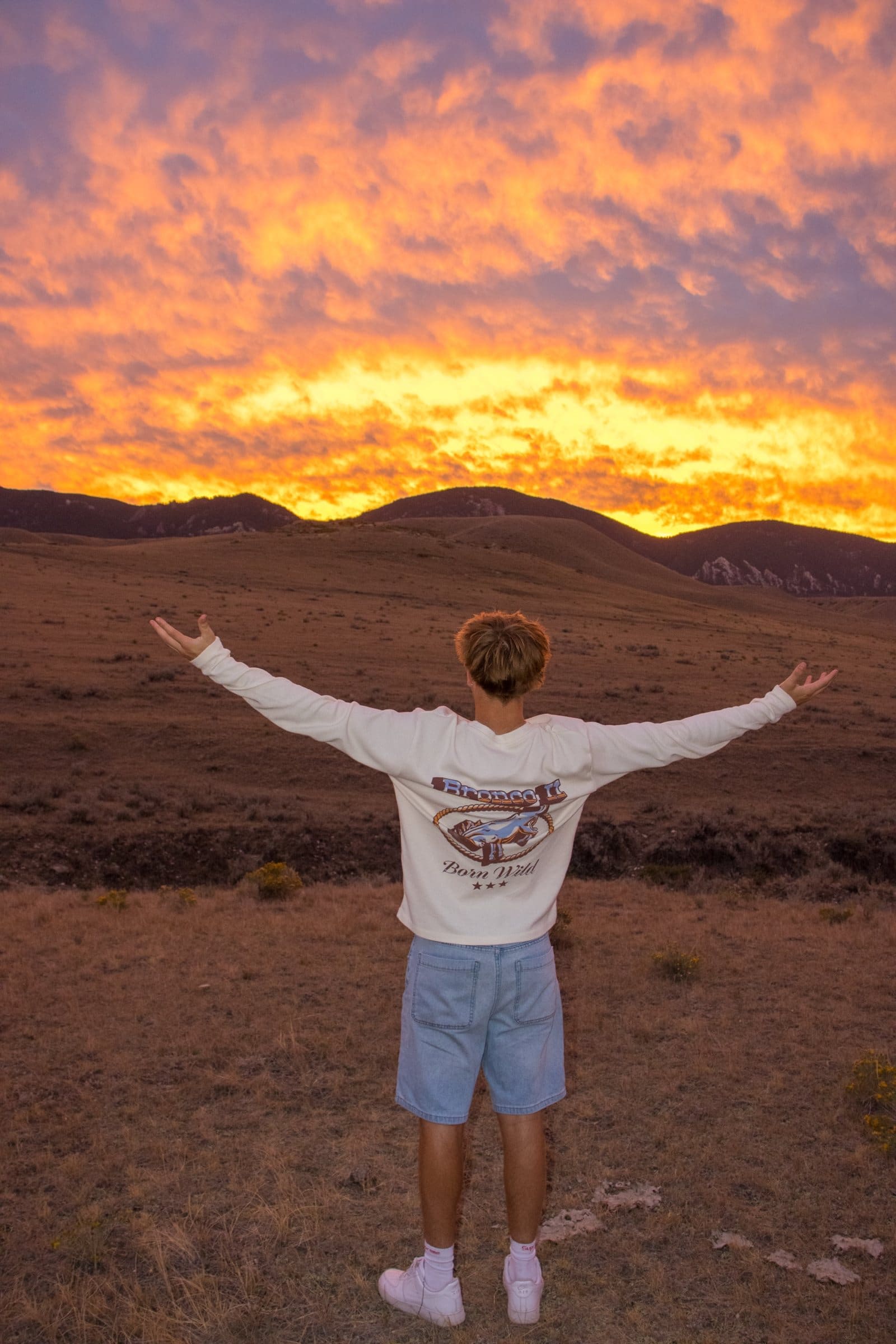 Senior portrait at sunset in the Bighorn foothills, arms open to a fiery sky