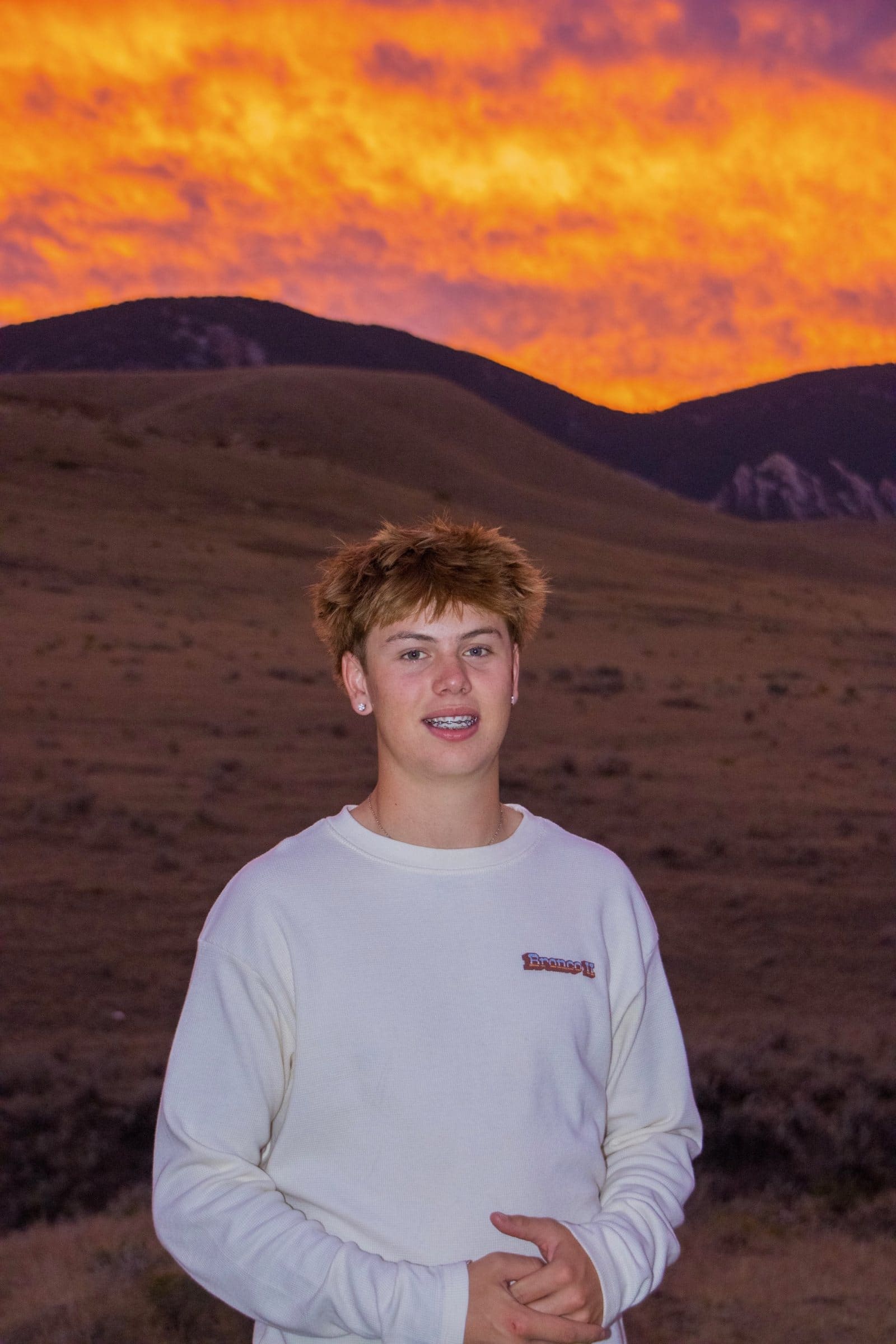 Smiling senior portrait in front of a glowing orange sky and mountains